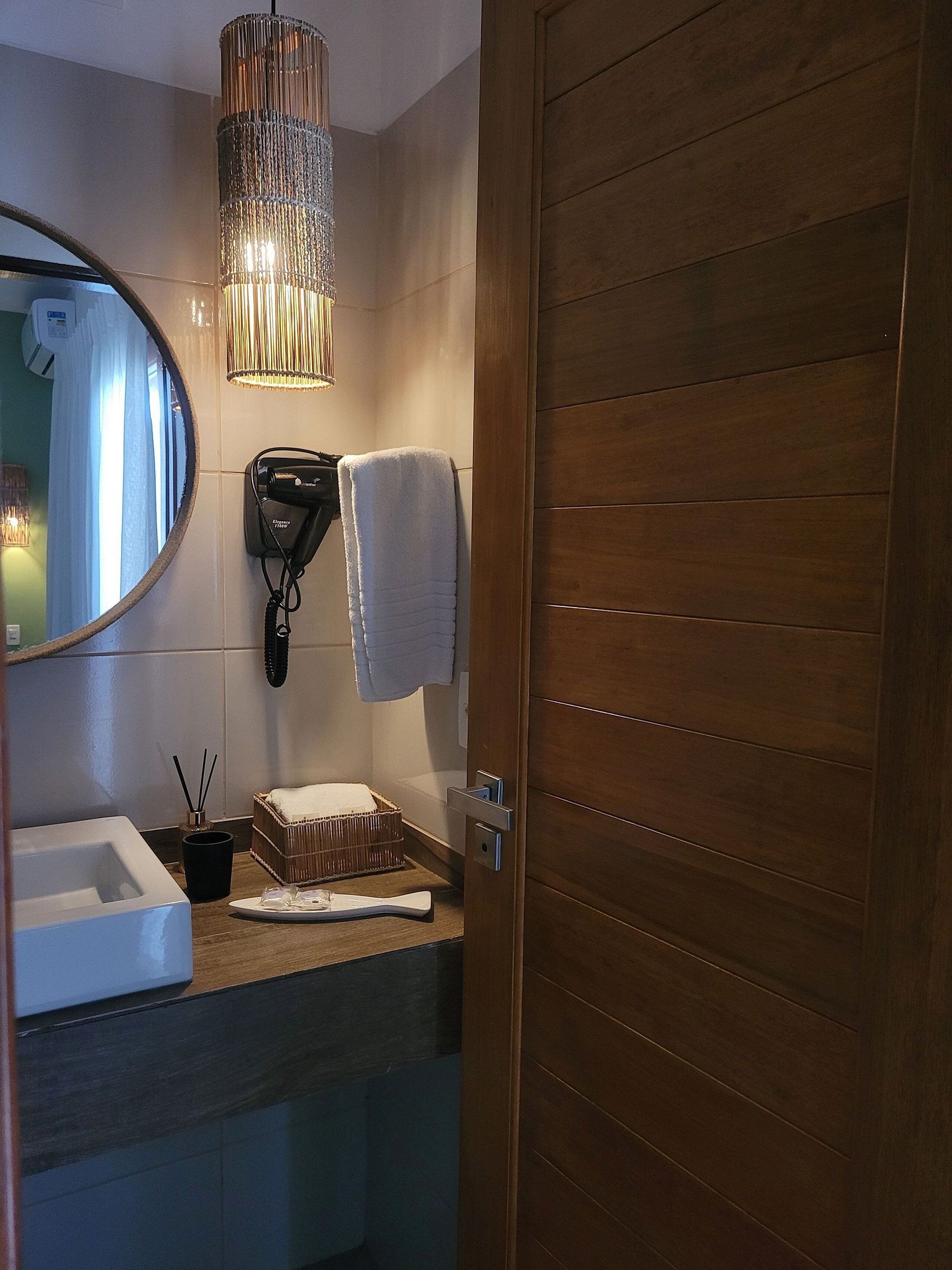 A bathroom with a wooden door, a mirror, a hairdryer, a towel, a bottle of shampoo, and a small basket.