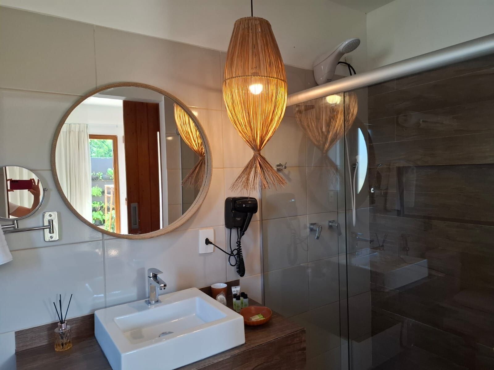 Ein modernes Badezimmer mit großem Spiegel, Waschbecken in Weiß, Fön und Duschkabine aus Glas.