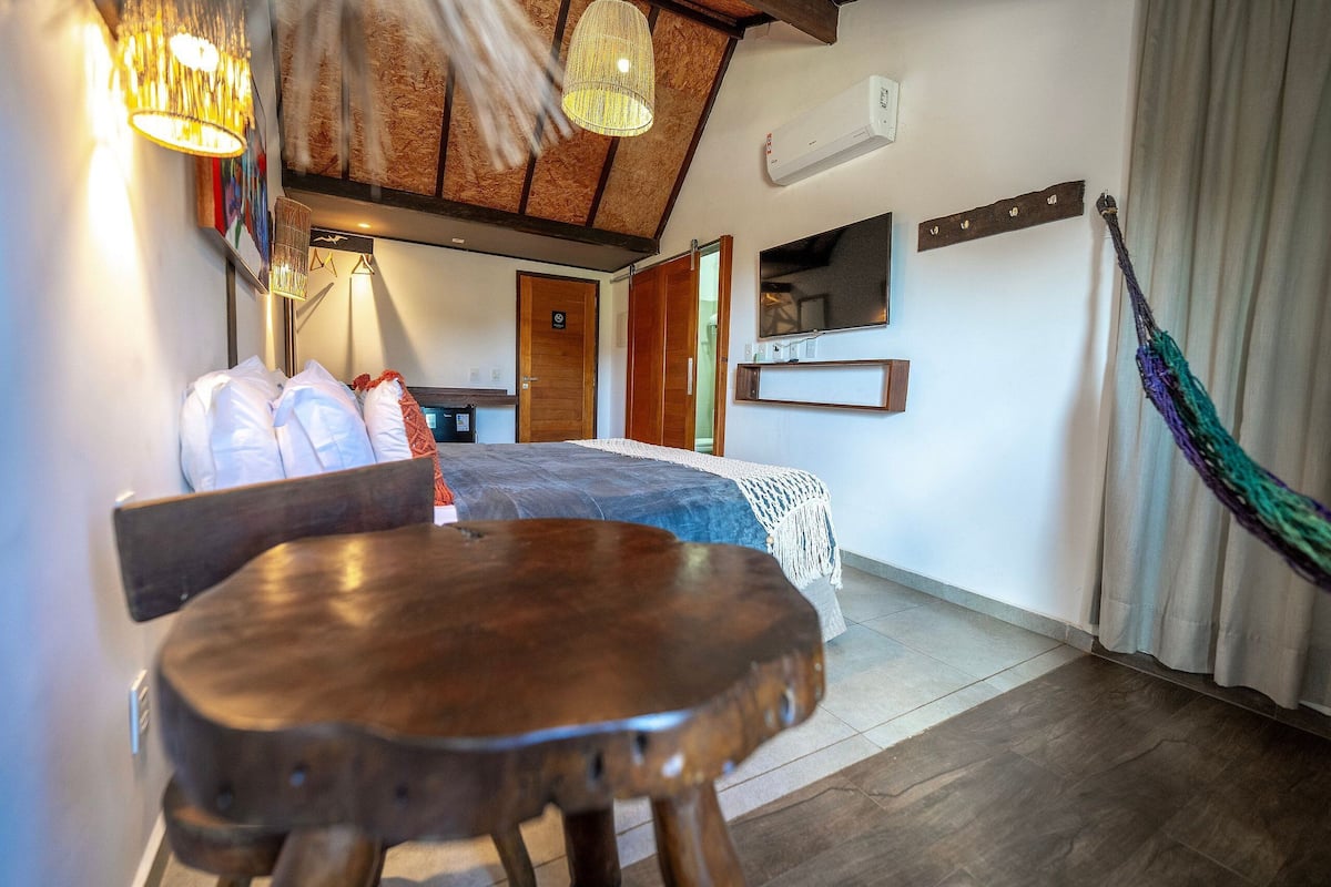 Une chambre avec un lit, une table en bois, un fauteuil suspendu, une télévision et un hamac.