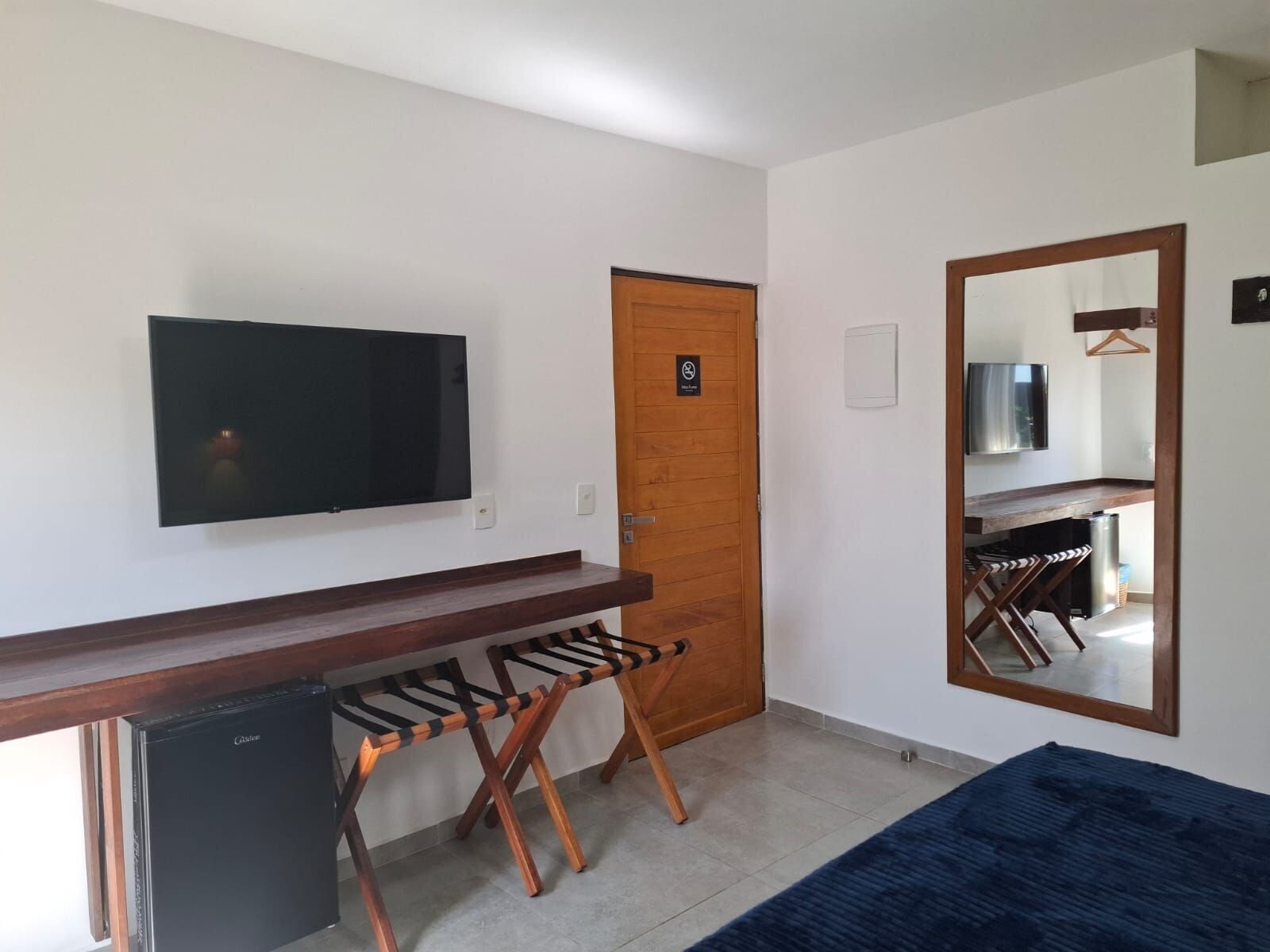 A room with a flat-screen TV mounted on the wall, a wooden door, a mirror, a small table, and a blue rug.