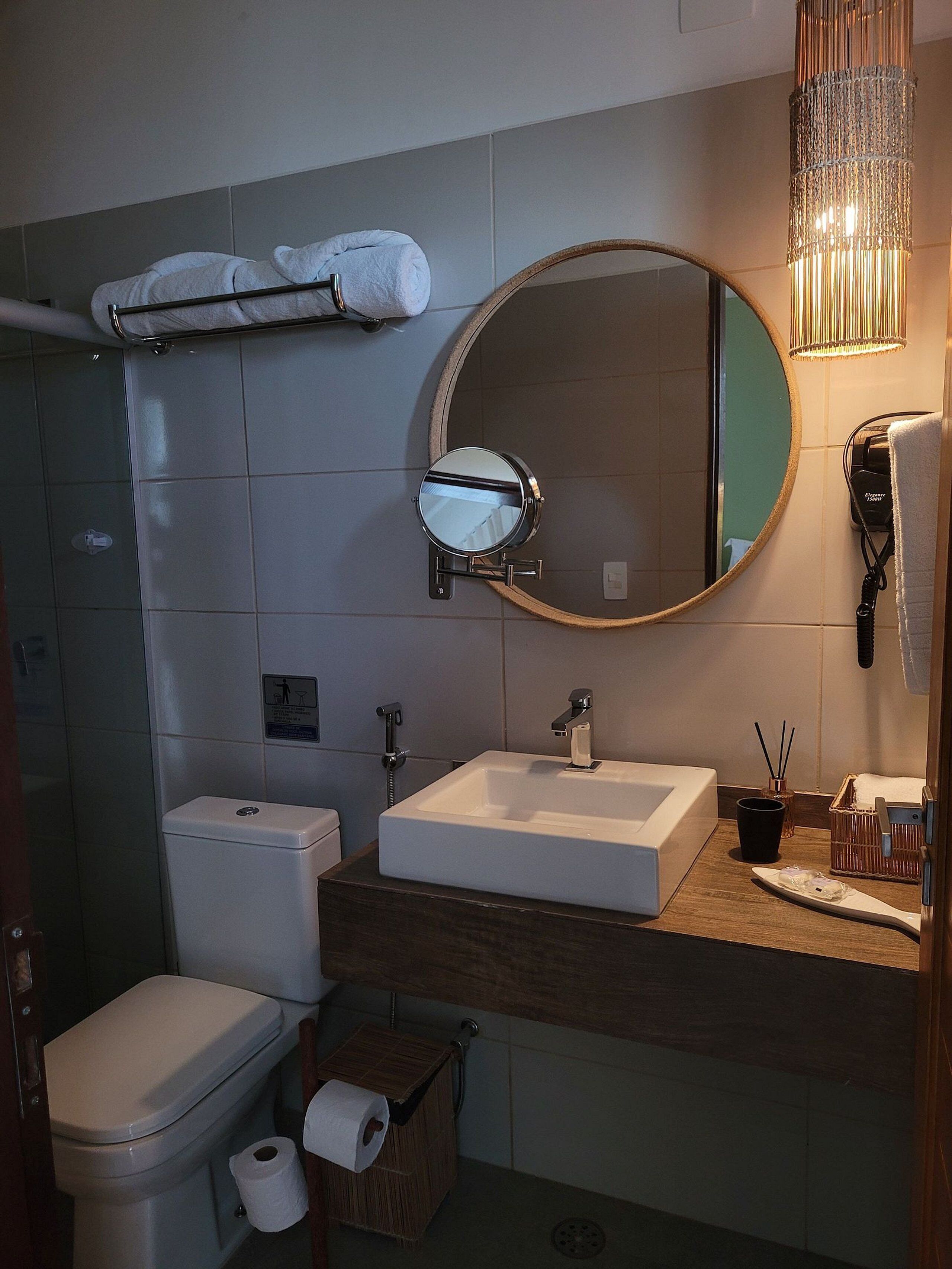 Ein Badezimmer mit Toilette, Waschbecken, Spiegel, Handtuchhalter und einem Fön.