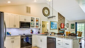 Una cocina moderna con armarios blancos, electrodomésticos de acero inoxidable, encimera de granito y una pared decorativa de piedra.