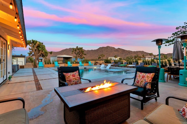 An outdoor pool area with lounge chairs, a fire feature, and a view of mountains.