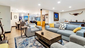 A modern living room with a sofa set, a coffee table, and a rug. There is a dining area with chairs and a table in the background. - Luxury 20-Acre Estate Pool, Spa, Game Room Sleeps 14 Near Joshua Tree NP (Joshua Tree)