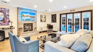 A modern living room with a fireplace, comfortable seating, artwork on the walls, and a view through large windows. - Luxury 20-Acre Estate Pool, Spa, Game Room Sleeps 14 Near Joshua Tree NP (Joshua Tree)