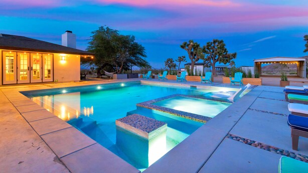 A swimming pool with a deck area, outdoor seating, and a building with large windows. - Luxury 20-Acre Estate Pool, Spa, Game Room Sleeps 14 Near Joshua Tree NP (Joshua Tree)