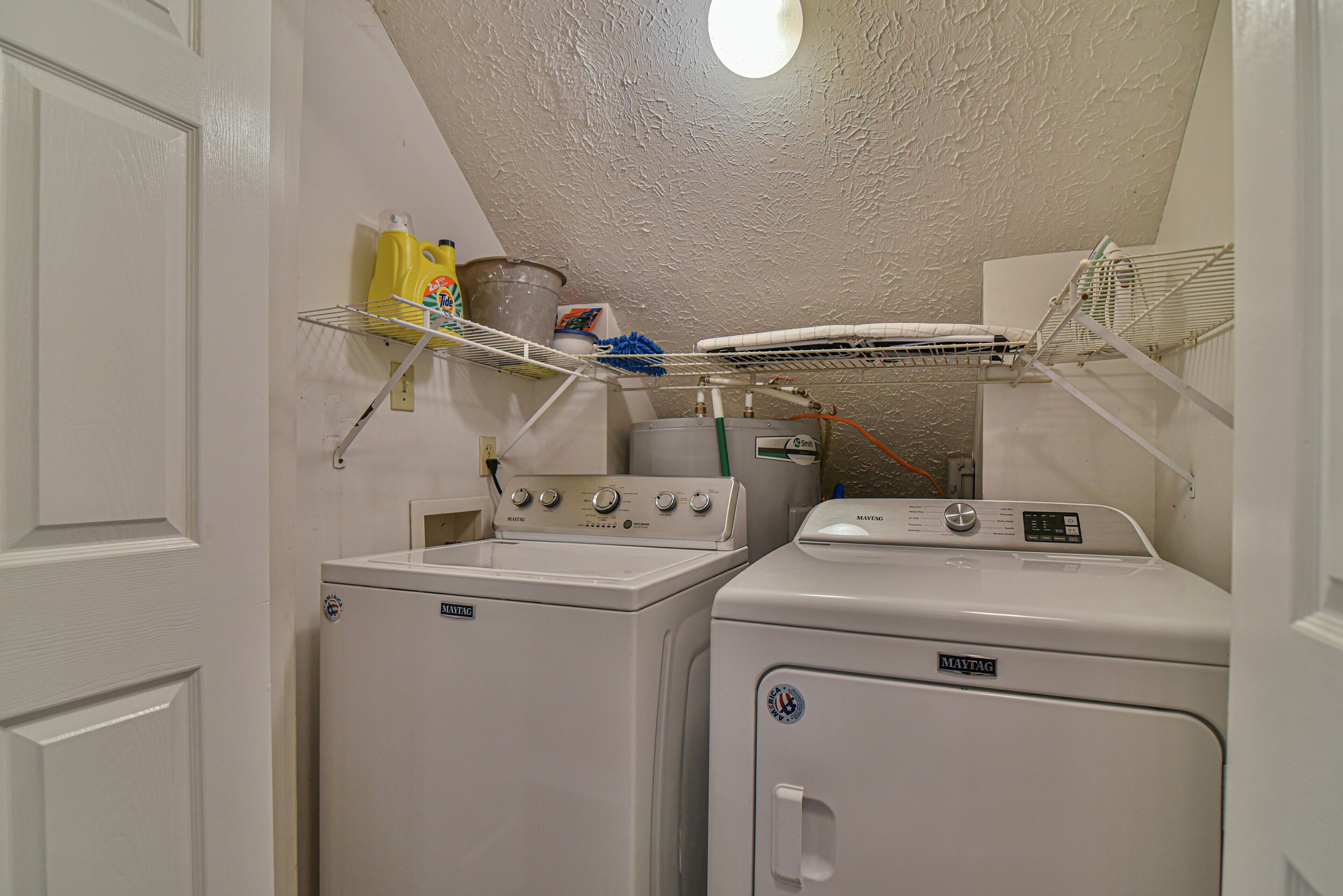 A laundry room with two washing machines, a drying rack, and a shelf with cleaning supplies.