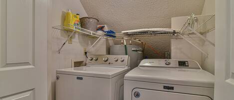 A laundry room with two washing machines, a drying rack, and a shelf with cleaning supplies.