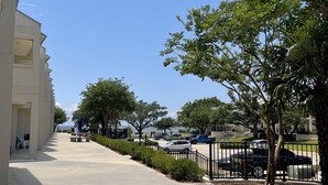Un large trottoir désert, avec un immeuble sur la gauche et une rue bordée d’arbres sur la droite.