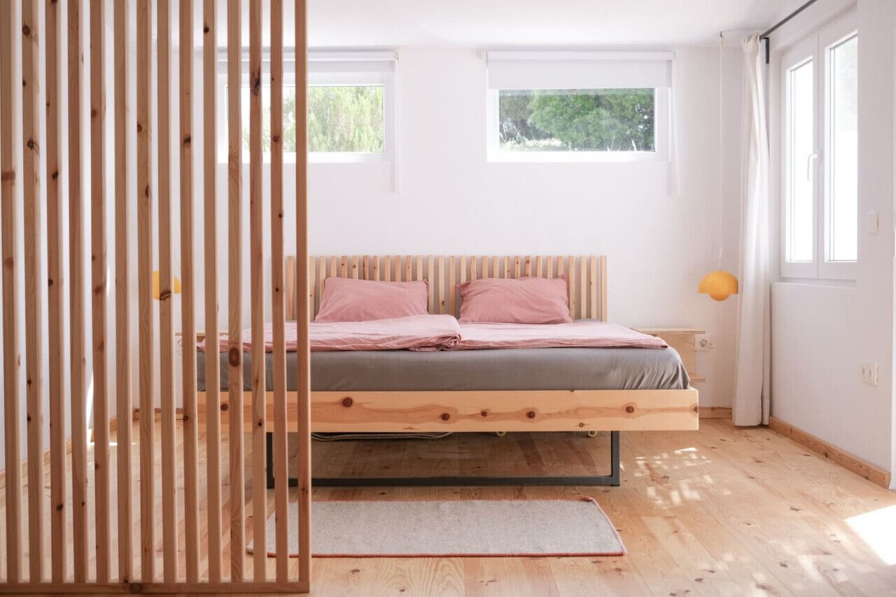 Une chambre à coucher au style minimaliste, avec un lit en bois, deux fenêtres et une vue sur la verdure.