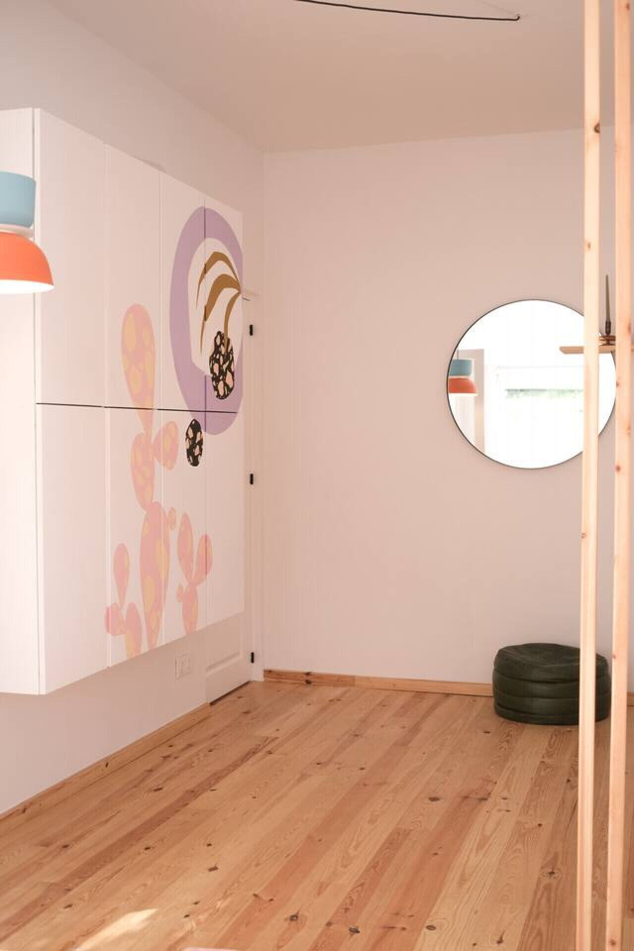 Une pièce avec un plancher en bois, une armoire blanche, un miroir rond et une petite table ronde.
