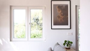 Een minimalistisch ingerichte kamer met een grijze bank, een lijst met een afbeelding en een potplant.