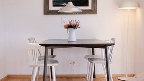 Een eethoek met een tafel, twee stoelen, een vaas met bloemen, een hanglamp en een lijst met een foto aan de muur.