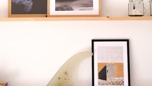 Een muur met drie ingelijste foto's: een strandgezicht, een zwart-wit abstract kunstwerk en een foto van een gebouw.