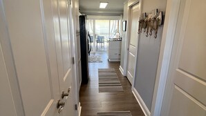Un couloir avec des portes blanches, un coin cuisine et une vue sur l’extérieur.