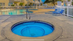Un espace piscine comprenant un jacuzzi, des chaises longues et une terrasse entourée d’une clôture.