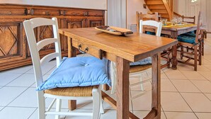 Ein Essbereich mit Holztisch, weißen Stühlen, einem Holzschrank und einer Treppe im Hintergrund.
