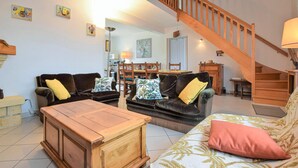 Ein Wohnzimmer mit Couchtisch aus Holz, zwei Sofas mit Kissen, einer Treppe und einem Essbereich mit Stühlen und Tisch.