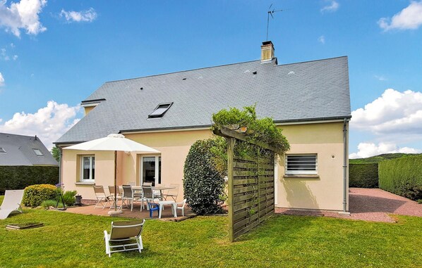 Ein zweigeschossiges Haus mit grauem Dach, einer kleinen Veranda mit Gartenmöbeln und einem gepflegten Rasen.