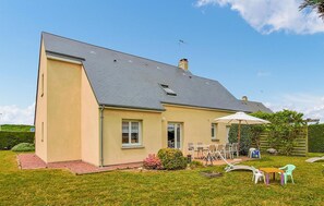Ein eingeschossiges Haus mit schrägem Dach, einer Haustür und einer kleinen Veranda mit Gartenmöbeln.