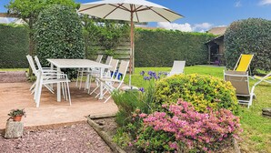Eine Terrasse mit Tisch und Stühlen, umgeben von einem Garten mit rosa Blumen und einer Hecke.