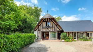 A traditional half-timbered building with a steeply pitched roof, a visible chimney, and a gravel driveway leading to a gated entrance. - Gorgeous home in Thierville (Thierville)
