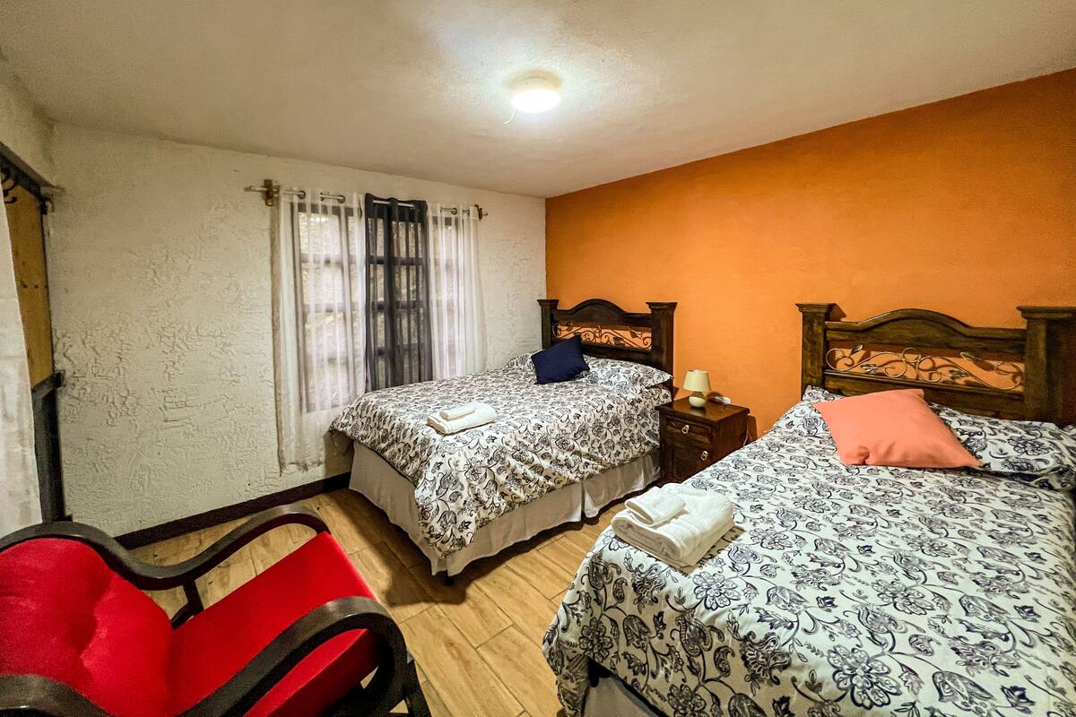 A room with two beds, a wooden chair, a nightstand, and a window with curtains.