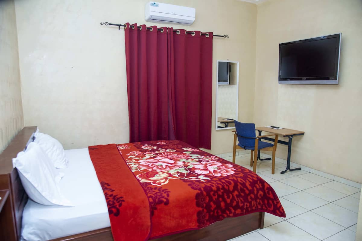 A hotel room with a bed, a desk, a chair, a TV, and a window with curtains.