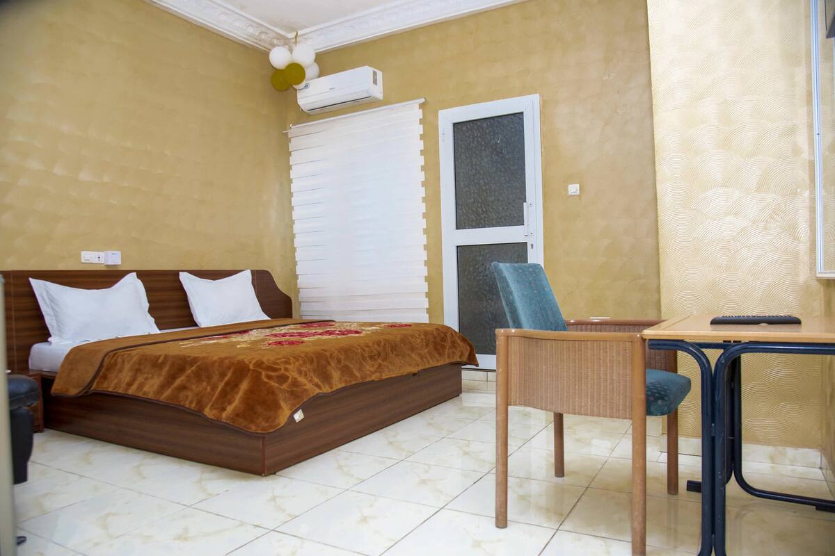 A bedroom with a bed, a desk, a chair, and a window with blinds.