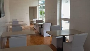 Et spiseområde med flere borde og stole, klinkegulv samt store vinduer der lukker naturligt lys ind.