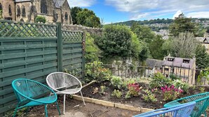 A garden with a wooden fence, two metal chairs, and a variety of plants.