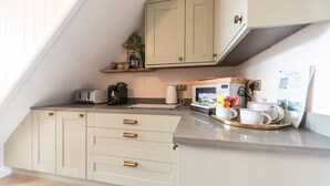 A compact kitchen with white cabinets, a microwave, a coffee maker, and a tray with cups and a teapot.
