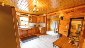 A wooden cabin interior with a kitchen area, wooden walls, and a dining table. - Secluded 3BR Cabin • Fire Pit • RV Parking • Near Tippy Dam & Big-M Trails (Wellston)