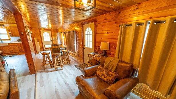 A cozy cabin interior with a wooden floor, leather sofa, dining table, and a kitchen area. - Secluded 3BR Cabin • Fire Pit • RV Parking • Near Tippy Dam & Big-M Trails (Wellston)