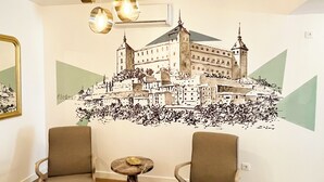A room with two armchairs, a small round table, and a wall mural of a castle. - ALCAZAR CERVANTES 5 COLLECTION (Toledo)