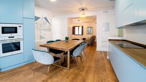 A modern kitchen with built-in appliances, a wooden dining table, and blue cabinetry. - ALCAZAR CERVANTES 5 COLLECTION (Toledo)
