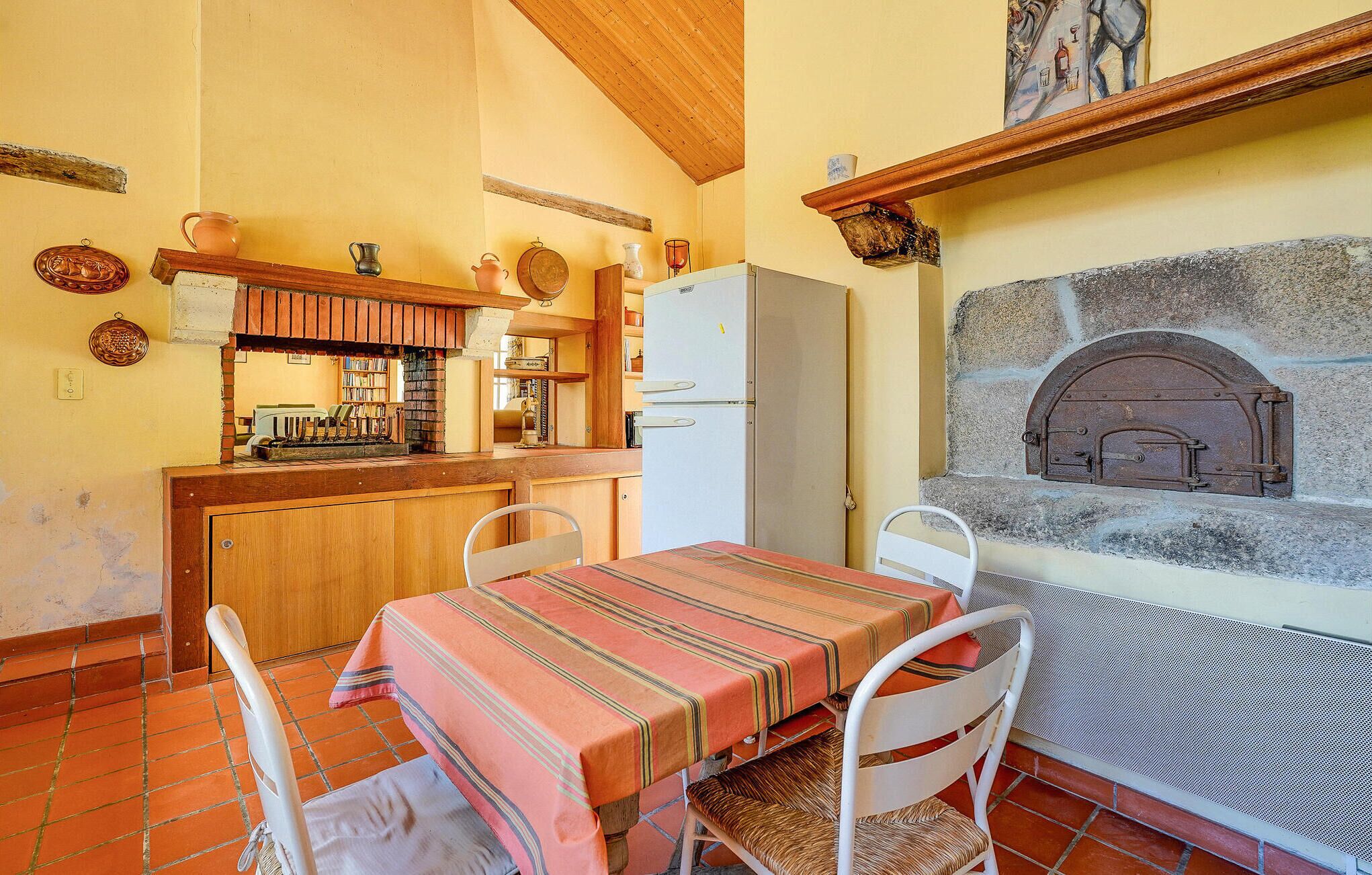 A kitchen with a stone oven, a refrigerator, and a dining table with chairs.