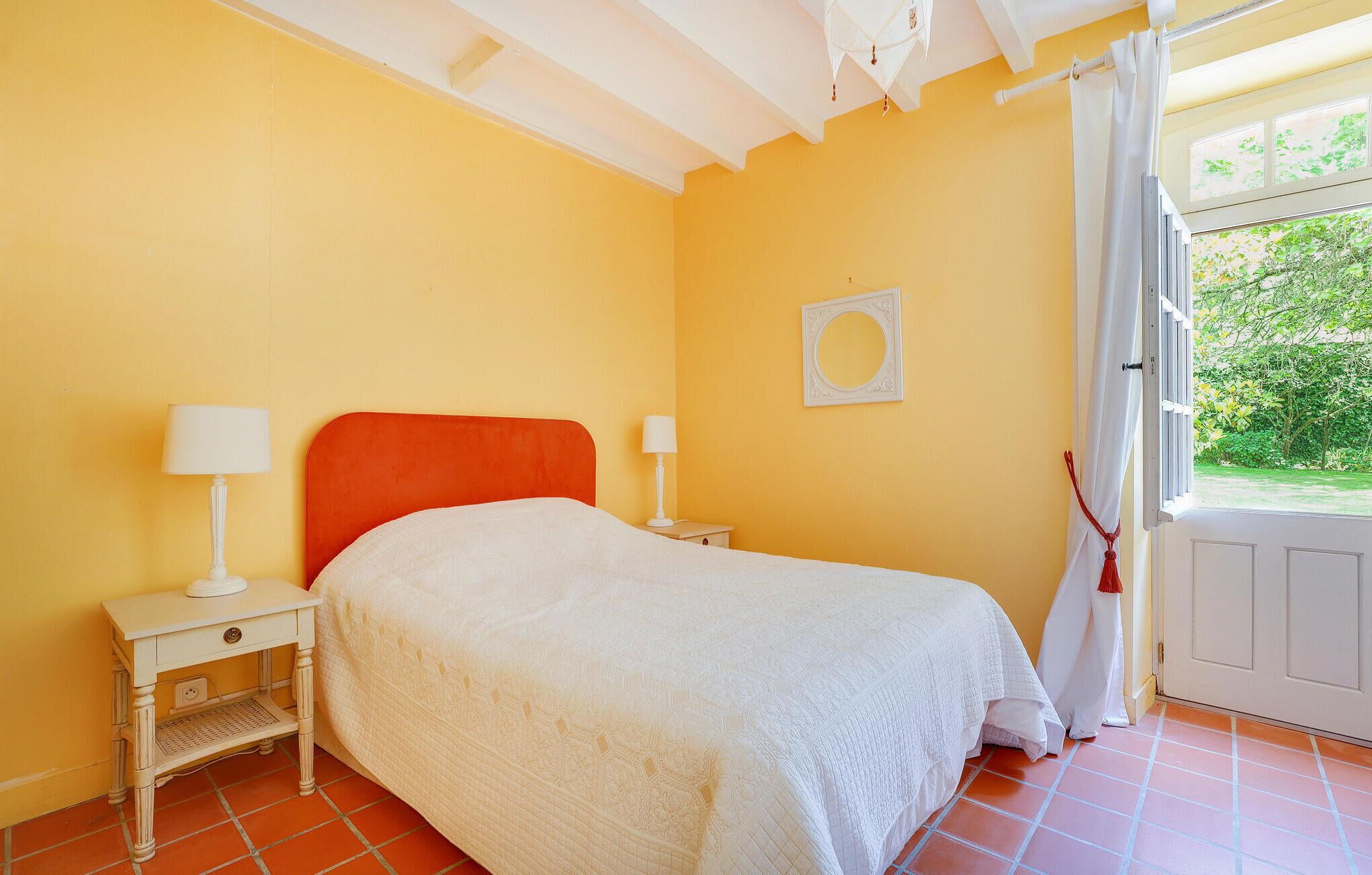 Un dormitorio con una cama, dos mesitas de noche, una mesita auxiliar, un espejo y una ventana con cortinas.