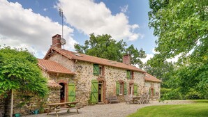 Een rustiek stenen huis met pannendak, groene luiken en een grindpad.