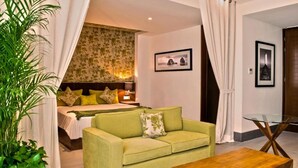 A hotel room with a bed, a green sofa, a wooden coffee table, and a dining table with chairs. - The Hamptons Studio
 (Bucerías)