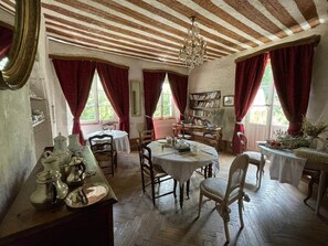 A dining room with a wooden ceiling, red curtains, a chandelier, and a bookshelf. - Château de Montanges Domaine du Très-haut, Piscine et Spa, Mariages/séminaires (Montanges)