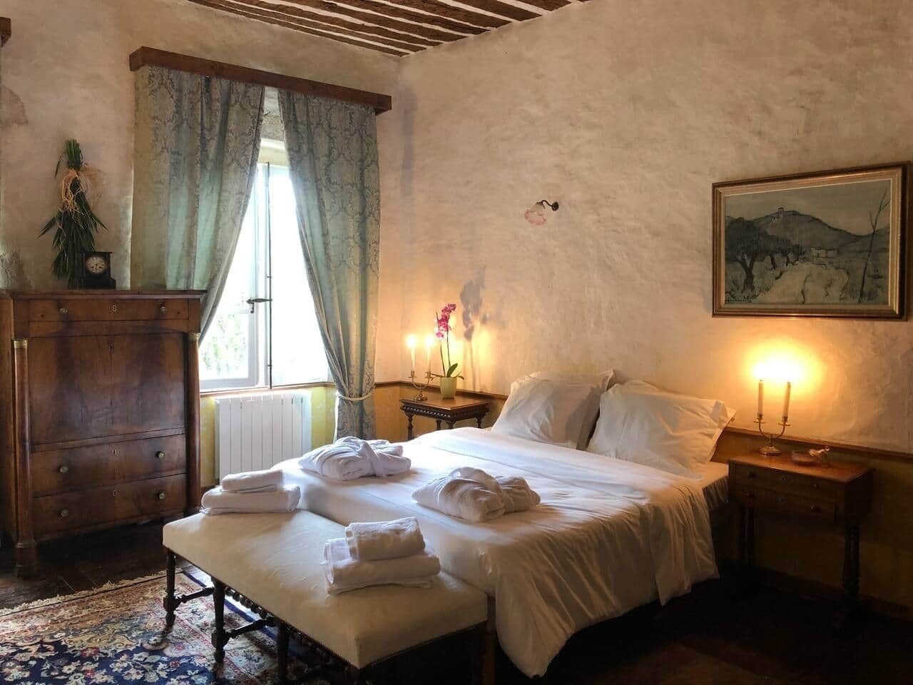 Un dormitorio con cama, mesitas de noche, cómoda, ventana con cortinas y un cuadro en la pared.
