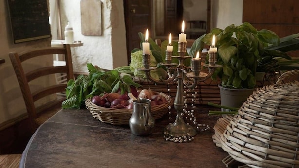 Una mesa rústica con un candelabro de velas, verduras frescas y una cesta de mimbre.