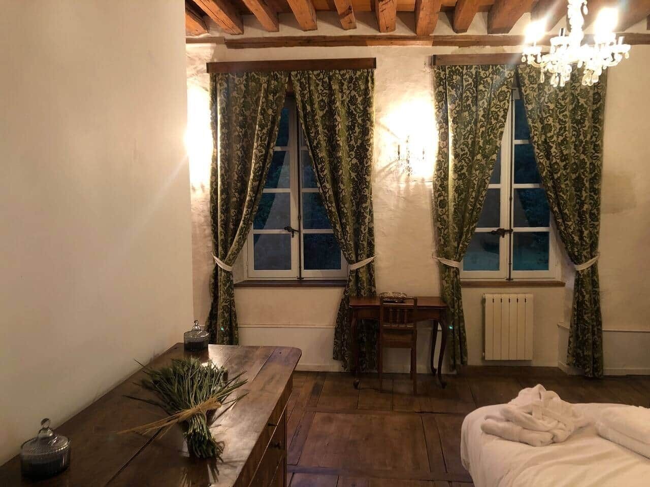A room with two windows, a wooden table, a bed, and a radiator.