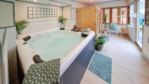A modern bathroom with a large bathtub, wooden paneling, and a seating area with a chair and table. - Lovely home in Thierville (Thierville)
