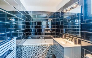 Une salle de bain moderne avec un grand miroir, une baignoire et un lavabo.