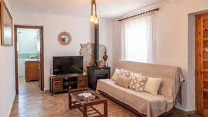 A living room with a sofa, coffee table, TV, fireplace, and a stone wall. - Casa Pulirio Antequera - La Higuera by Ruralidays (Málaga)