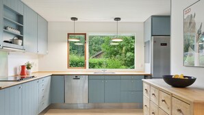 Une cuisine moderne avec des meubles de couleur bleu clair, un plan de travail en bois, un lave-vaisselle, un évier à deux bacs et une grande fenêtre donnant sur un espace verdoyant.