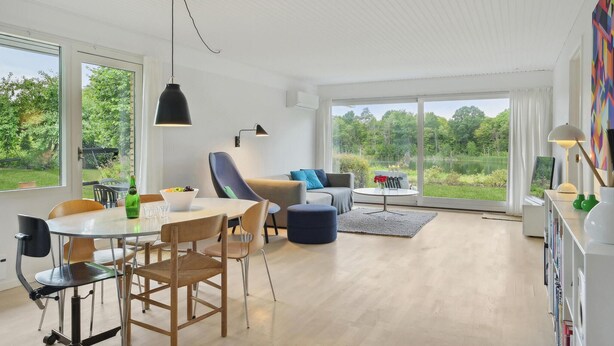 Un salon moderne avec un coin repas, de grandes fenêtres et une vue sur un lac.