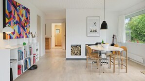 Un salon moderne comprenant un coin repas, une bibliothèque, un tableau et une fenêtre donnant sur un paysage verdoyant.